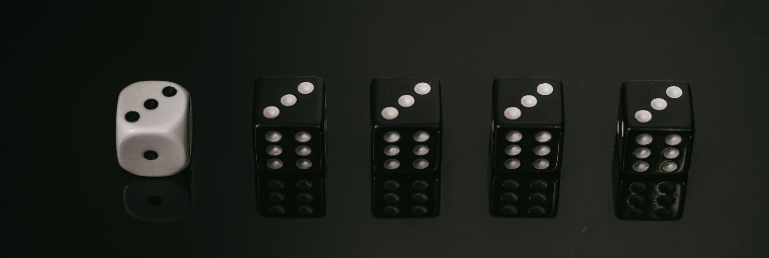 Fünf Würfel, ein weißer und vier schwarze, liegen in einer Linie auf schwarzem Hintergrund und symbolisieren App Store Optimierung.